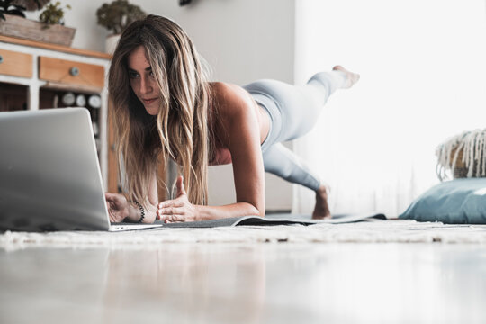Fit and healthy lifestyle young woman doing plank position at home looking a lesson on the laptop. Sport and active workout on the web. Following internet channel about body positivity and health