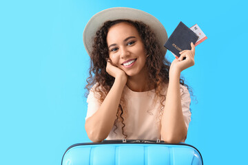 Young African-American woman with passport and suitcase on blue background
