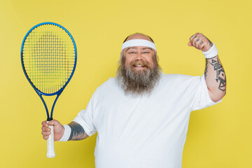 happy and overweight tennis player showing win gesture and looking at camera isolated on yellow.