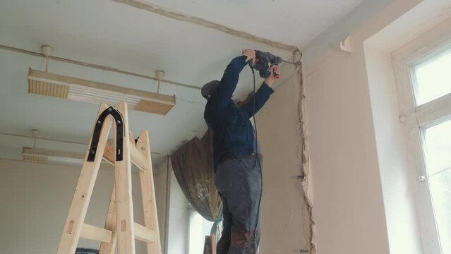 The master builder drills a hole in the wall during the repair work in the room. Recovery and restoration of the room. A male electrician drills a track in a concrete wall for laying a cable.