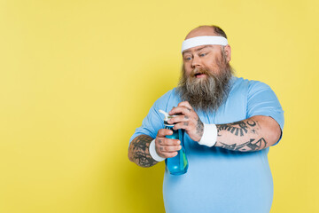 thirsty overweight man with beard opening sports bottle isolated on yellow. - obrazy, fototapety, plakaty
