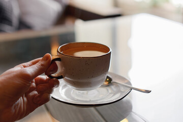 Closeup of female hands with french manicure holding cozy ceramic white mug of tea or coffee. Relax and comfort at home, cafe. Drinking hot cocoa. Empty space for text on blurry background, banner