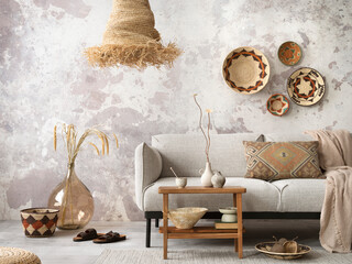 The stylish ethnic composition at living room interior with grey sofa, colorful wicker, straw lamp,...