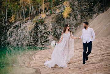 Newlyweds near a beautiful lake. Middle Eastern groom and Caucasian bride walking along the coast.