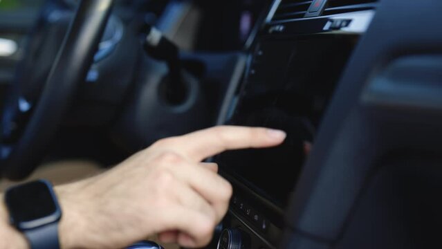 Unknown young man sitting in front of the handlebar of his own luxury auto and applying navigator. Male man hand touching, tapping, zoom out on screen monitor on modern luxury car. Interface concept