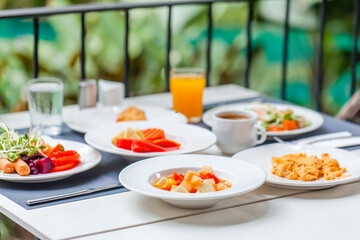 Buffet breakfast on terrace in outdoors restaurant at tropical hotel or resort. Brunch table with food and drinks, fried eggs, coffee cup, fruits. Summer holidays, vacations, tourism, travel concept.