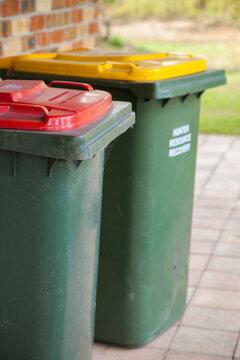 Rubbish and recycling bins beside the brick wall of a home