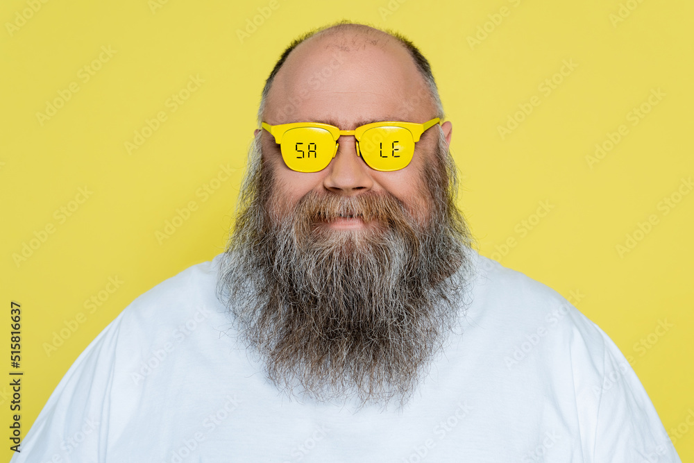 Wall mural smiling plus size man with beard wearing glasses with sale lettering isolated on yellow.