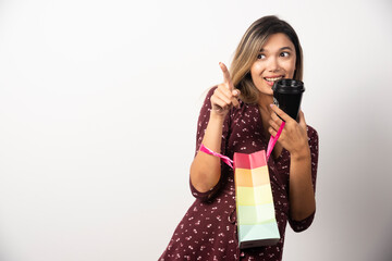 Young woman holding a small shop bag and a cup of drink on white background