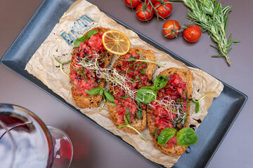 a bruschetta with tomatoes on a dark table, a glass of red wine