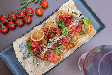 a bruschetta with tomatoes on a dark table, a glass of red wine