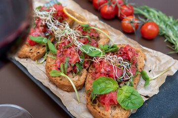 a bruschetta with tomatoes on a dark table, a glass of red wine