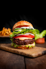 Burger with beef meat, cheese, lettuce, onion, tomato, cucumber, mayo and ketchup on an old wooden table. Junk food concept