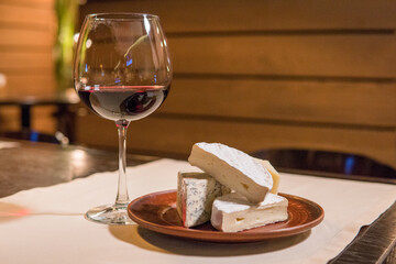 A glass of red wine and a head of cheese on a plate