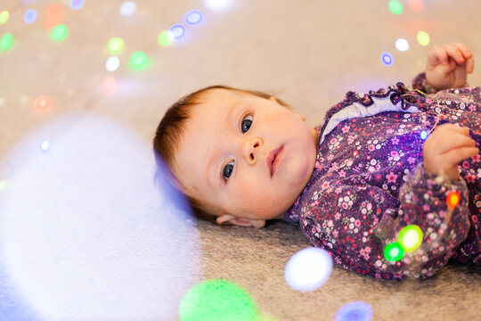 Young baby on floor holding colourful Christmas fairy lights