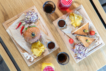 Beef patty burger, bacon, cheese, tomato, greens, pickle, goose pate sandwich, red cabbage salad, hot pepper, fries, corn chips, ketchup, orange and cherry juice