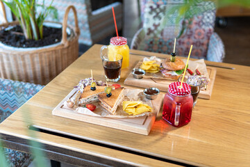 Beef patty burger, bacon, cheese, tomato, greens, pickle, goose pate sandwich, red cabbage salad, hot pepper, fries, corn chips, ketchup, orange and cherry juice