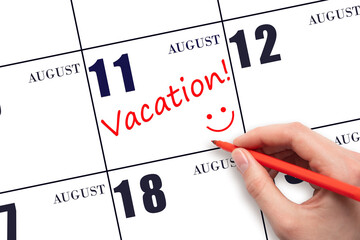 A hand writing a VACATION text and drawing a smiling face on a calendar date 11 August. Vacation...