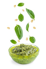 Green healthy homemade italian pesto sauce served in glass bowl with flying or levitating ingredients such as fresh basil leaves, pine nuts, olive oil, garlic and parmesan isolated on white background