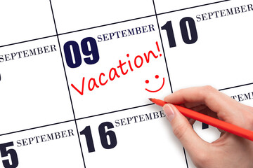 A hand writing a VACATION text and drawing a smiling face on a calendar date 9 September . Vacation planning concept.