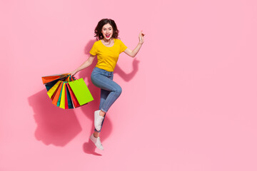 Full size photo of impressed young brunette lady jump with bags wear t-shirt jeans sneakers isolated on pink background