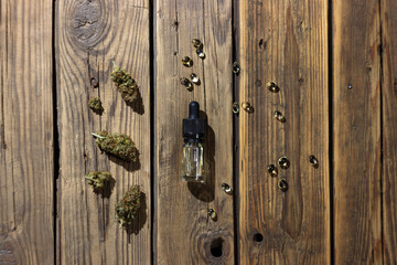 Medical cbd oil in a glass bottle with a pipette, surrounded by dry marijuana buds and cbd extract in capsules.  On a wooden background.  View from above