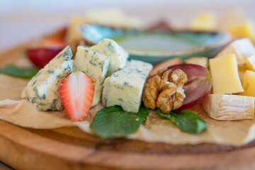 Cheese assorted with honey, decorated with fresh fruits, strawberries, grapes, lemon, walnut