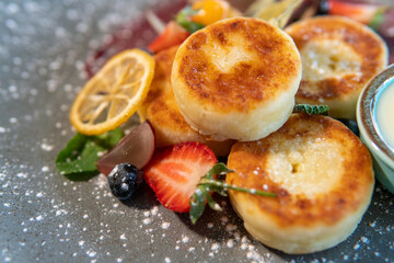 Cheesecakes with condensed milk and strawberries on a gray plate standing on a dark table
