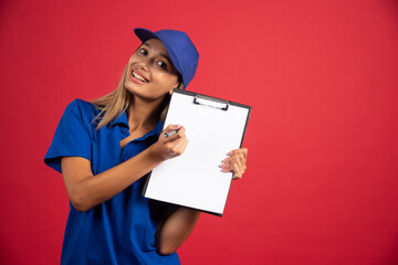 Young woman in blue uniform pointing at clipboard with pencil