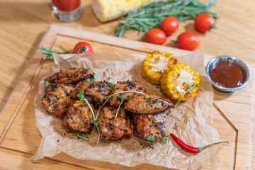 Chicken wings with barbecue sauce, hot pepper, microgreens, corn, tomato juice on a wooden board