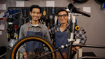 Portrait of Asian senior man and son owner bicycle shop smiling and looking at camera in bicycle workshop
