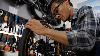 Asian senior man owner repairing and checking wheels and gears of bicycle while standing in bicycle shop