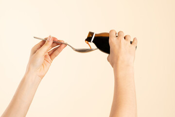 Image of hands with table spoon and bottle of medication. Pouring cough syrup or cold liquid medication into spoon. Bottle with no label. - obrazy, fototapety, plakaty