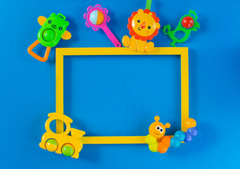 Fototapeta premium Children's toys rattles on a blue background and a yellow text frame. Top view, flat position. The concept of child development. Place to copy.
