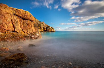 Scenic landscape of a small beach on the coast of Cartagena, Spain, taken with long exposure in which the colors of the rocks, the sea and the sky stand out