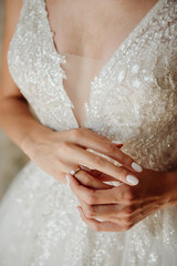 Hands of the bride in a white wedding dress with a gold engagement ring with a diamond close-up