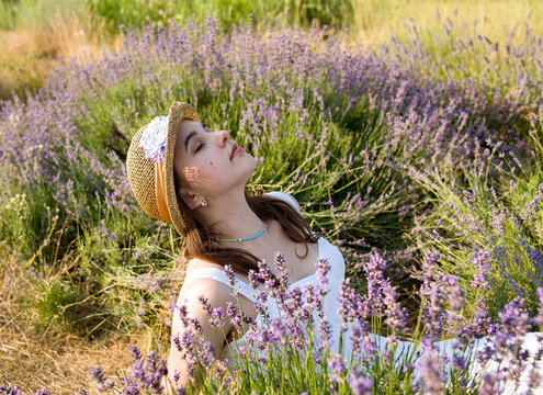 portrait of a beautiful sexy smoling woman with closed eyes in straw hat sniffing violet flowers in lavender field