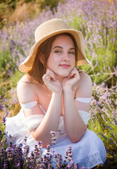 portrait of a beautiful sexy smiling woman  in straw hat and white dress dreaming in lavender field