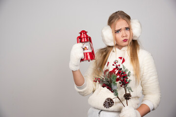 Puzzled woman holding holly berries and Christmas lamp