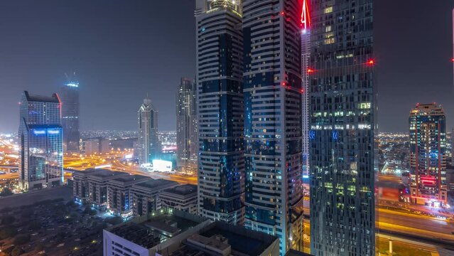 Aerial panorama of Dubai International Financial District with many skyscrapers during all night timelapse. Traffic on a road junction and Sheikh Zayed road with lights turning off. Dubai, UAE.