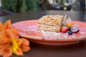 Napoleon cake classic on an orange plate with fresh strawberries and physalis