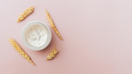 Natural cosmetic concept. Open jar with cream and wheat on pink pastel background. Flat lay, copy space. Minimal. Organic product for skin care.