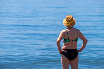 Senior woman standing alone in front of the Mediterranean sea at a beach in a sunny summer day.