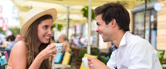Young smiling couple drinking coffee on coffee shop terrace on a sunny summer morning