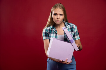 Blonde girl holds tight a gift box and looks confused and dissatisfied