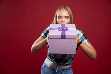Blonde girl holds tight a gift box and looks confused and dissatisfied