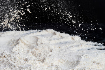 Flying white flour, powder on a black background. Spray of particles, lumps, pieces of white...