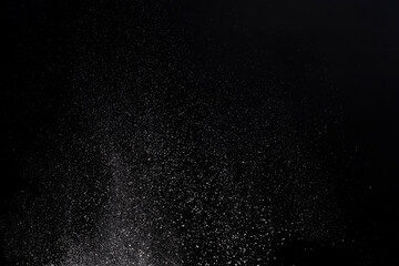 Flying white flour, powder on a black background. Spray of particles, lumps, pieces of white matter.Sweeping dry dust, paint, farina