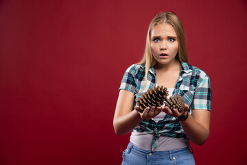 Blonde girl holds oak tree cone in the hand and gives surprized poses