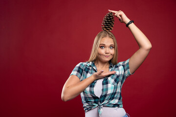 Blonde girl holds oak tree cone at her head and feels positive